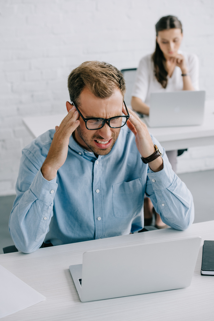 wysoki kąt widzenia biznesmena w okularach cierpiących ból głowy podczas pracy z laptopem w biurze - Zdjęcie, obraz