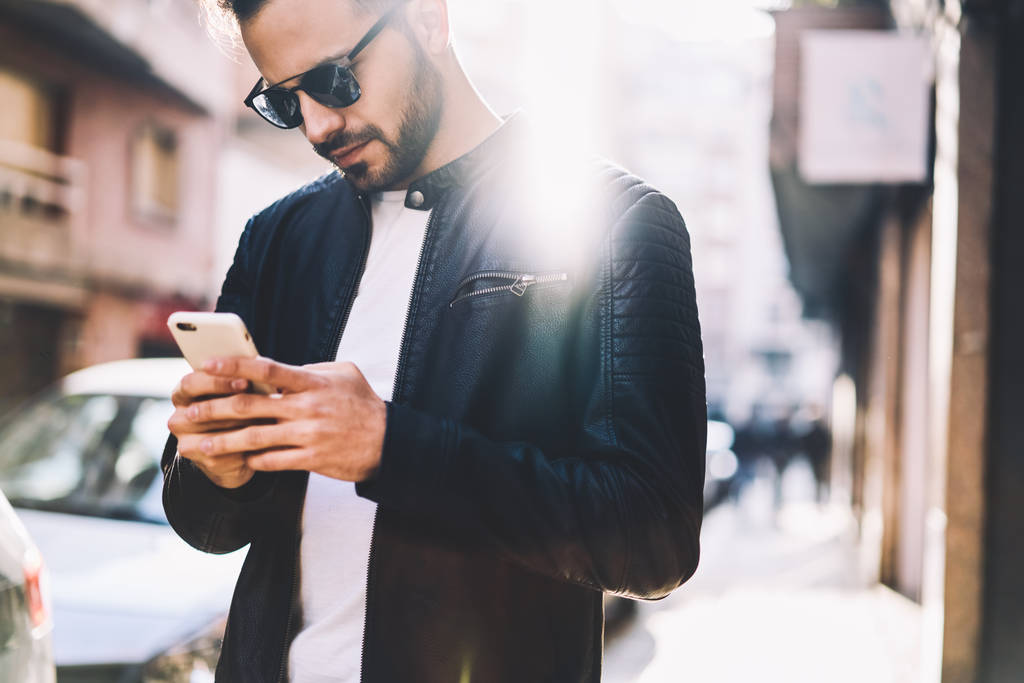 Jovem masculino verificando notificação e notícias de leitura no smartphone andando na rua da cidade, cara hipster bonito usando o aplicativo bancário no celular moderno ao ar livre para fazer o pagamento on-line facilmente
 - Foto, Imagem