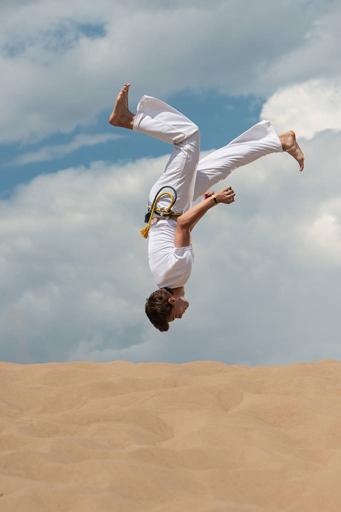 Acrobat performs an acrobatic trick, somersault on the beach. Man trains capoeira - Photo, Image