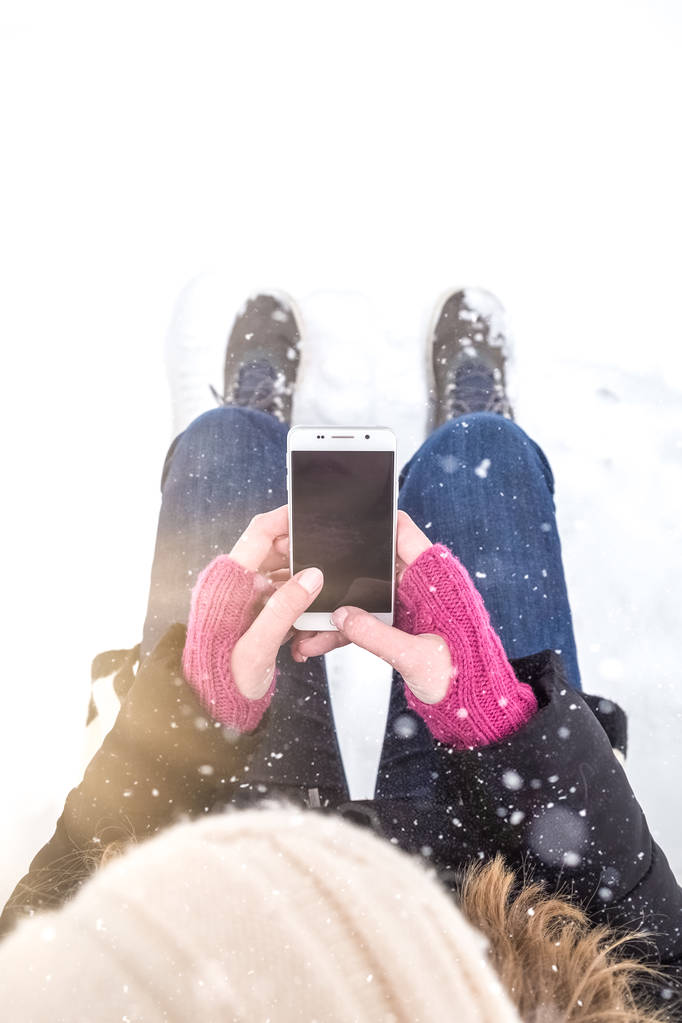 Visão de alto ângulo da fêmea segurando telefone inteligente tela em branco contra fundo de neve branca
. - Foto, Imagem