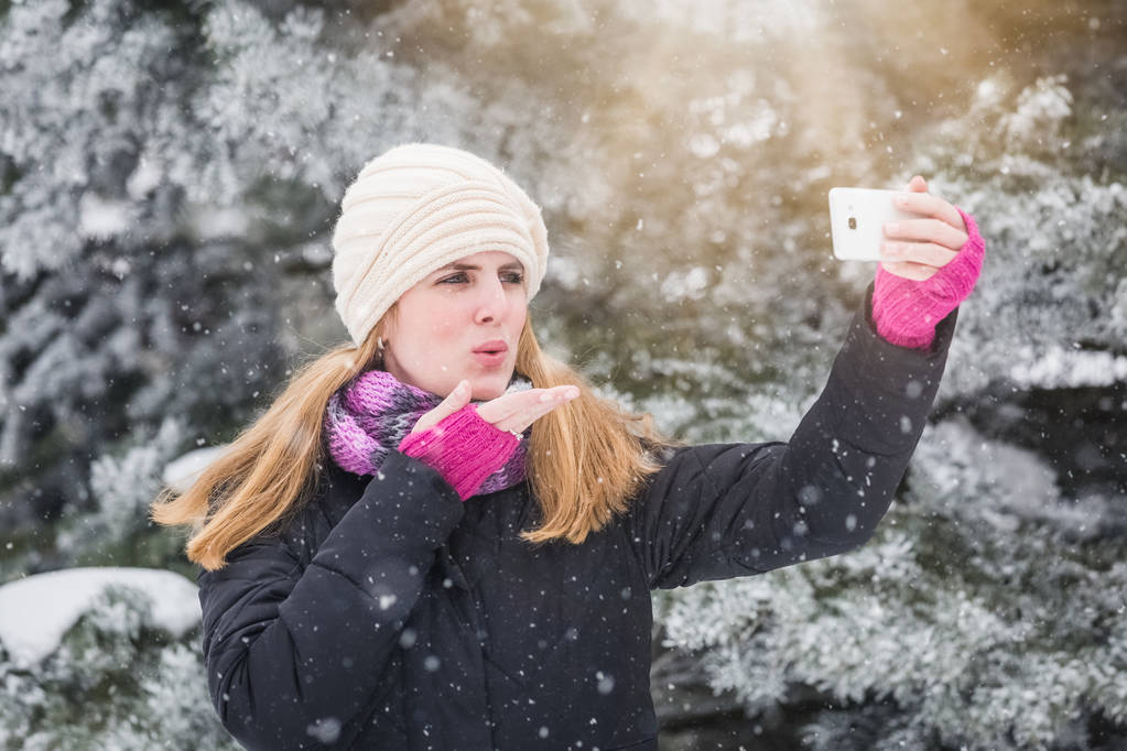 Ευτυχισμένη γυναίκα λαμβάνοντας αυτοπορτρέτα πέρα από το υπόβαθρο του χειμώνα. - Φωτογραφία, εικόνα