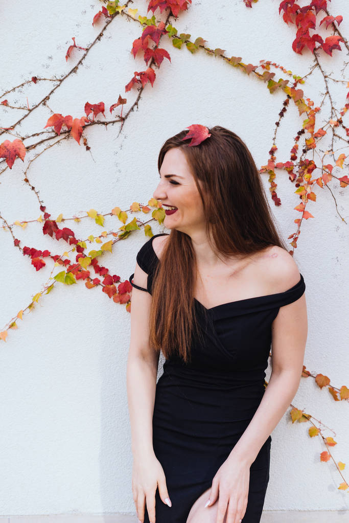 Πολυτελές μακρυμάλλης γυναίκα σε ένα όμορφο μαύρο φόρεμα θέτοντας ενάντια στον τοίχο και το γέλιο - Φωτογραφία, εικόνα