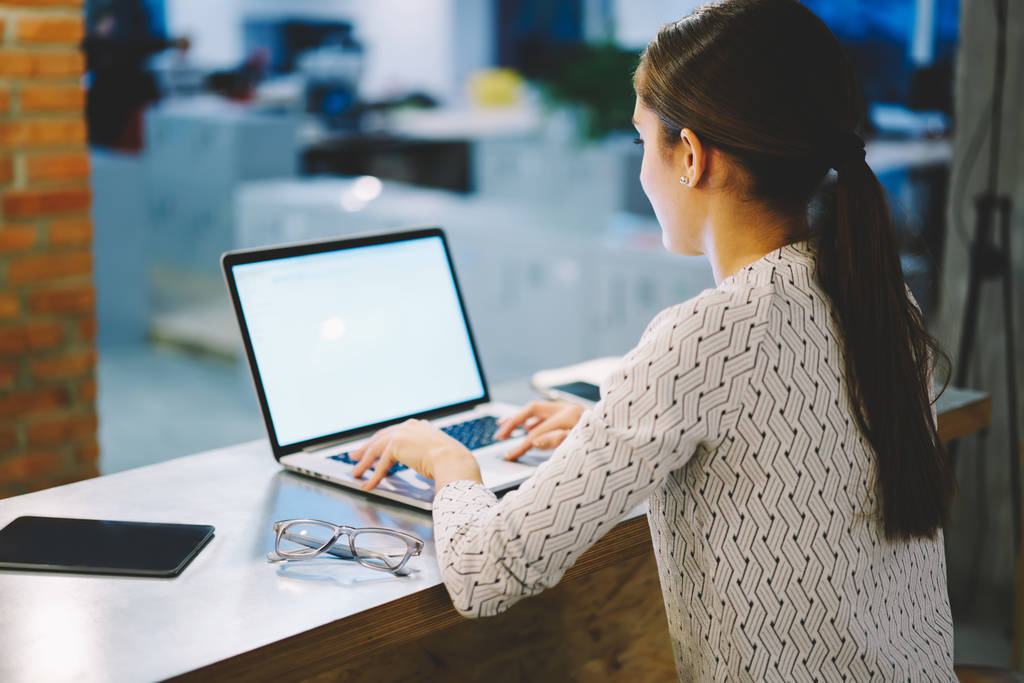 Powrót widzenia pracownica pisania na komputerze przenośnym z makiety ekran pobierania multimediów i wyszukiwanie wyszukiwanie informacji w Internecie; kobieta siedzi w miejscu pracy w biurze przy użyciu netbook - Zdjęcie, obraz