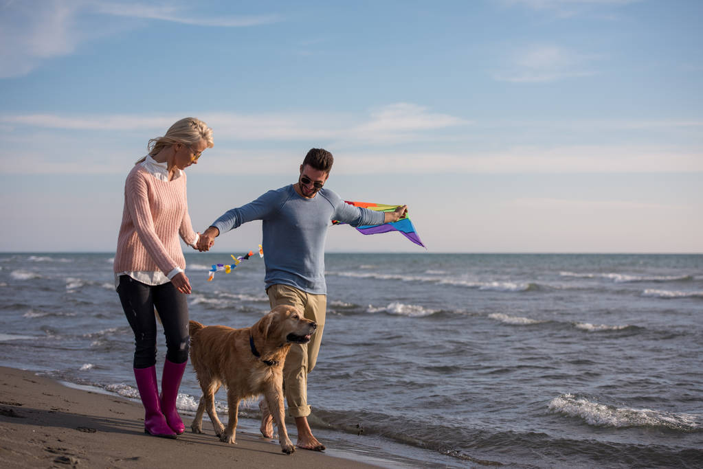 Fiatal pár szórakozik játék-val egy kutya és a Kite a strandon, őszi nap - Fotó, kép