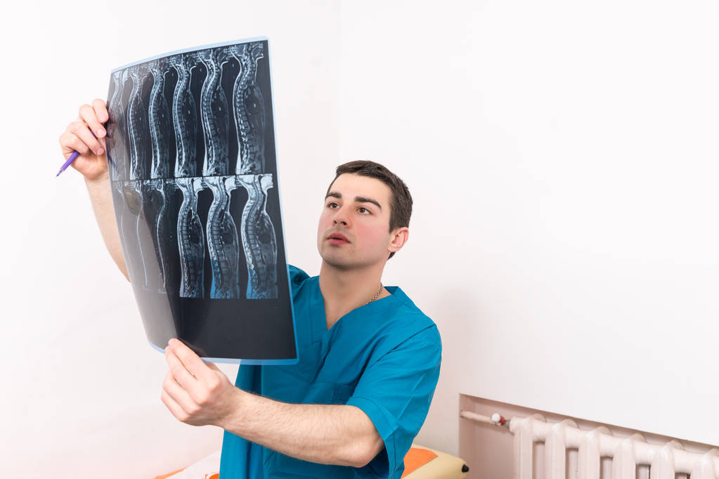 Fisioterapeuta o médico que mira una radiografía ortopédica de una columna vertebral humana que la sostiene mientras la examina
 - Foto, imagen