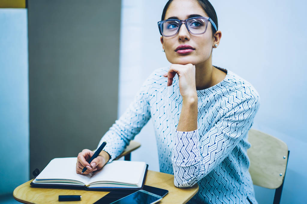 Στοχαστικός γυναίκα σε γυαλιά για διόρθωση της όρασης υπενθυμίζοντας πληροφορίες κατά την εγγραφή δοκιμή στην τάξη κολέγιο, συλλογισμένος φοιτήτριας ΣΚΕΨΕΙΣ για δουλειά εργασία μάθηση κάθεται στο γραφείο - Φωτογραφία, εικόνα