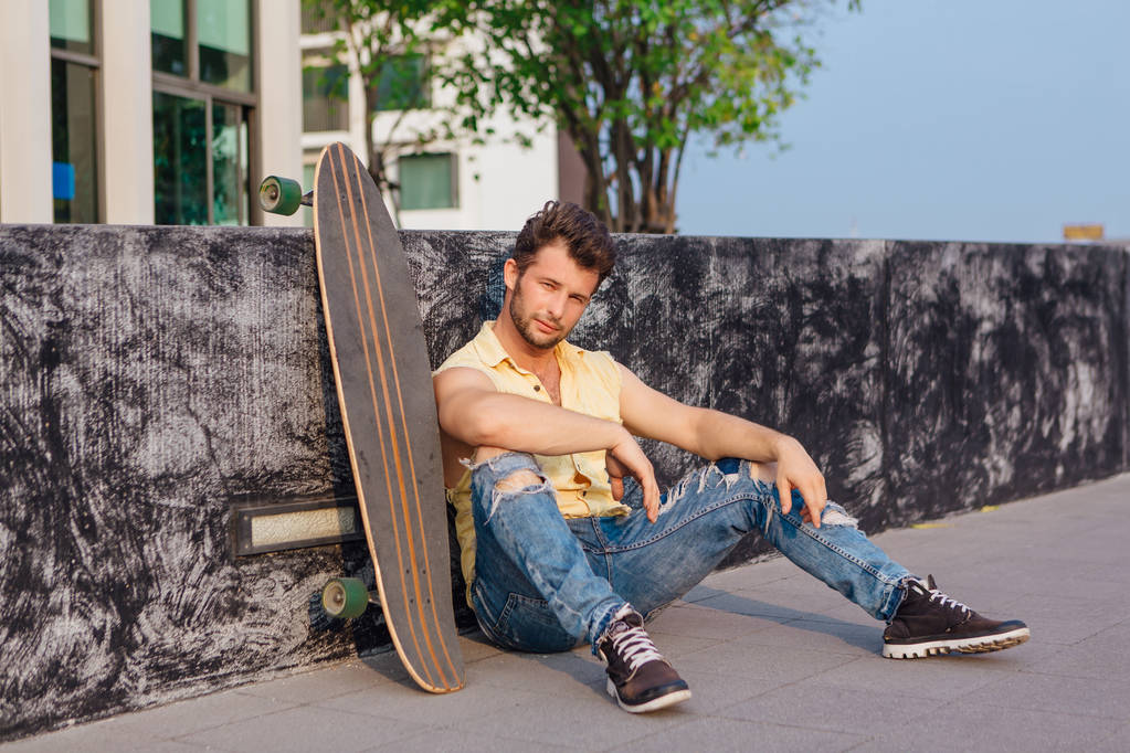 Joven hombre guapo con barba sentado con longboard en la calle
. - Foto, imagen