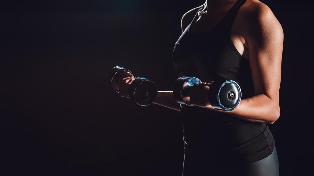 cropped image of female athlete exercising with dumbbells, black background  - Photo, Image