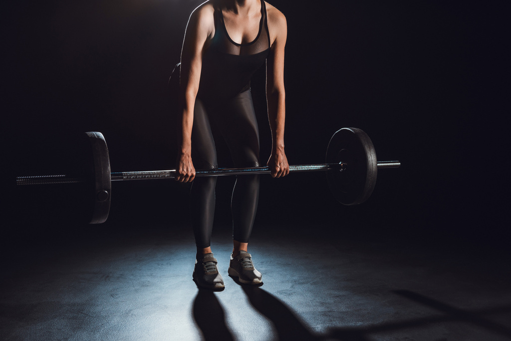 περικομμένη εικόνα αθλήτρια που κάνει άσκηση με barbell στο γυμναστήριο, μαύρο φόντο - Φωτογραφία, εικόνα