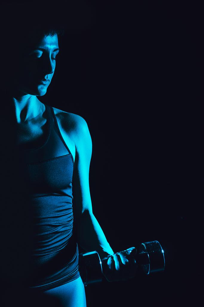 toned picture of sportswoman doing exercise with dumbbell, black background  - Photo, Image