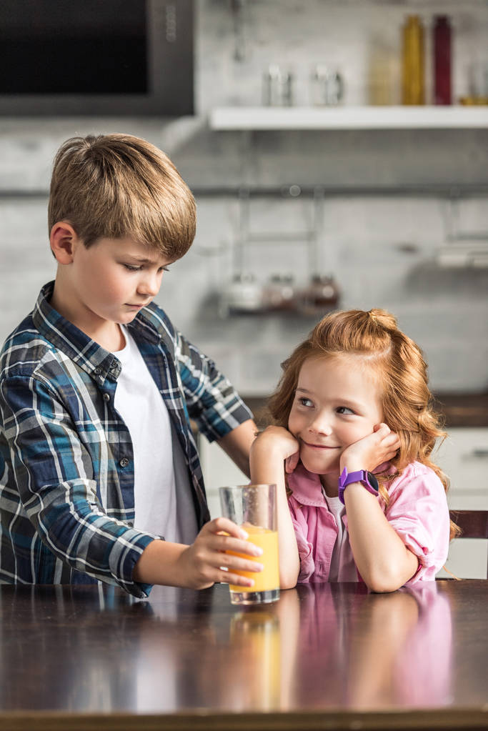 Очаровательный младший брат, дающий стакан апельсинового сока своей улыбающейся сестре
 - Фото, изображение