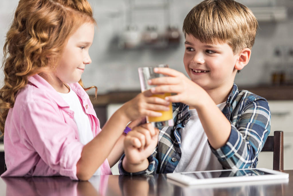 little brother and sister passing glass of orange juice at kitchen - Photo, Image