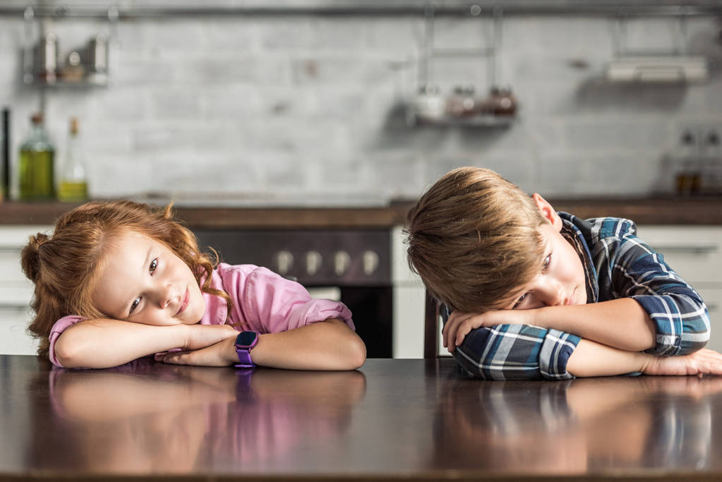 уставшие младшие брат и сестра лежат на столе и смотрят в камеру
 - Фото, изображение