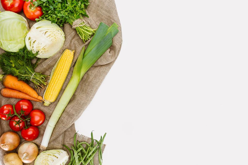 σύνθεση των τροφίμων με φρέσκα λαχανικά που διοργανώνονται σε λινάτσα απομονωθεί σε λευκό - Φωτογραφία, εικόνα