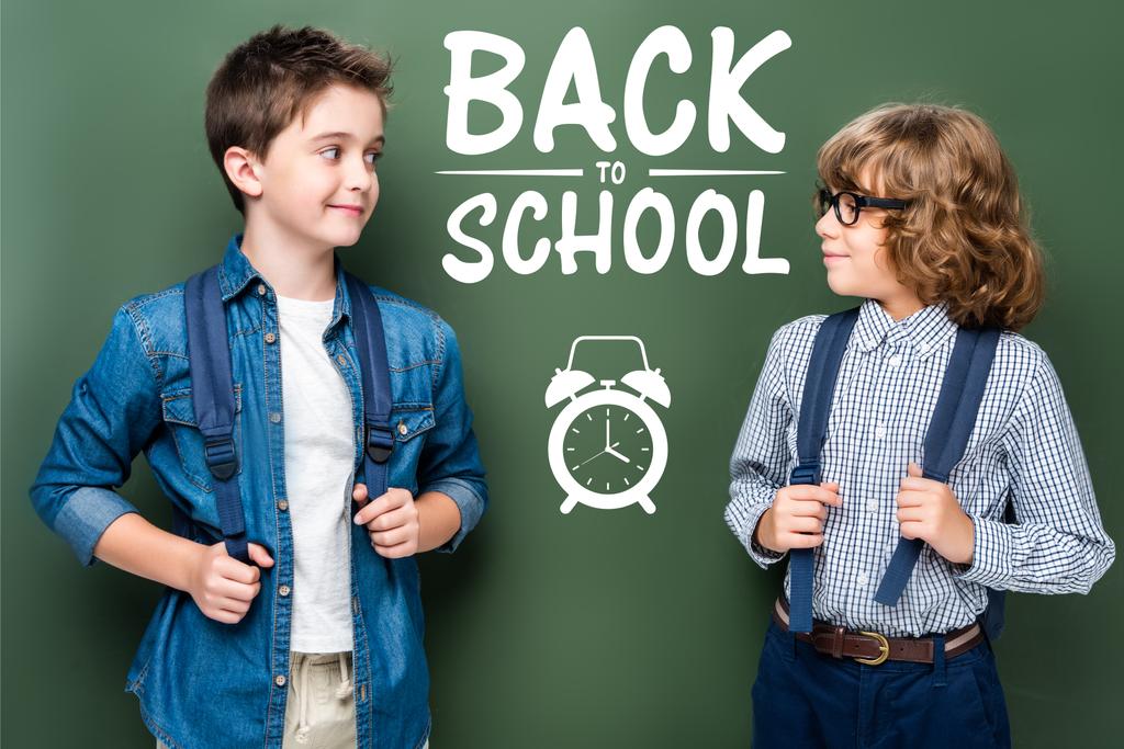 目覚まし時計と「学校に戻る」レタリング黒板近く見てお互いバックパックでの男子生徒 - 写真・画像