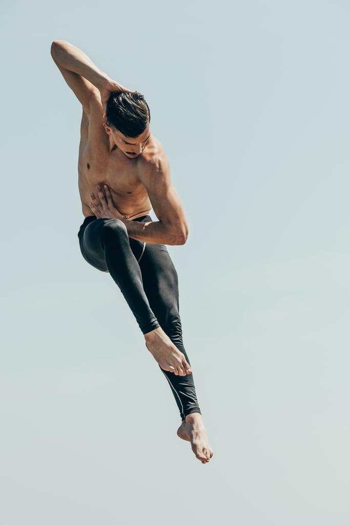 рухомий знімок красивої без сорочки танцівниці в стрибку проти блакитного неба
 - Фото, зображення