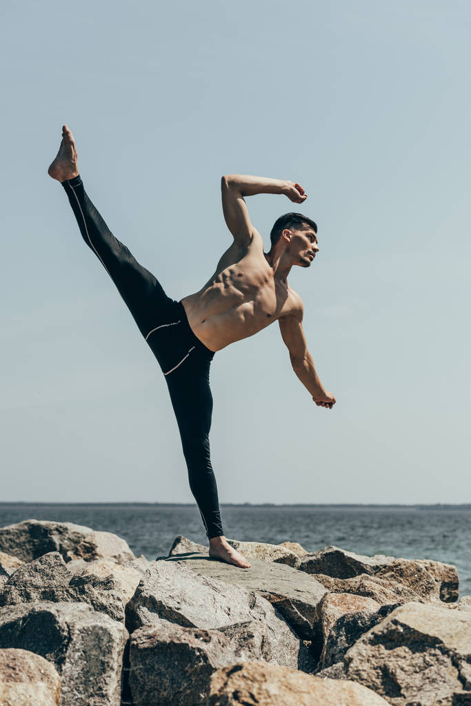 jóképű félmeztelen férfi tánc a sziklás tengerpart - Fotó, kép