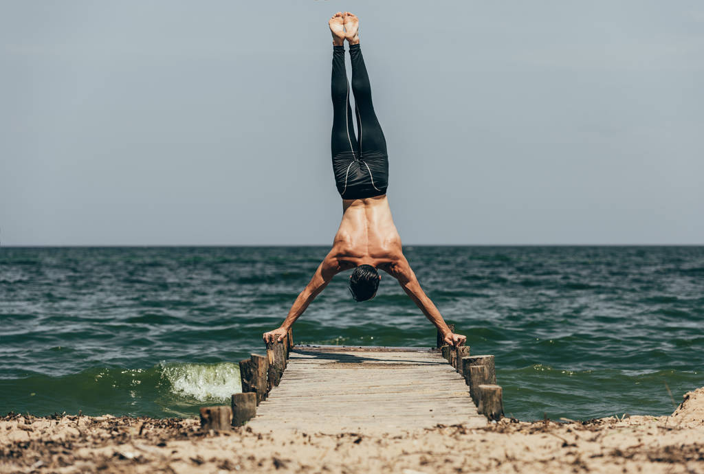 knappe shirtless man uitvoeren handstand op houten pier - Foto, afbeelding