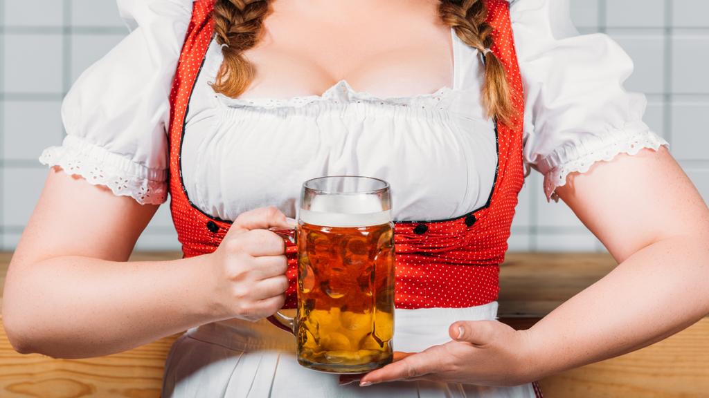 bijgesneden afbeelding van oktoberfest serveerster in traditionele Duitse kleding bedrijf mok licht bier in de buurt van toog - Foto, afbeelding