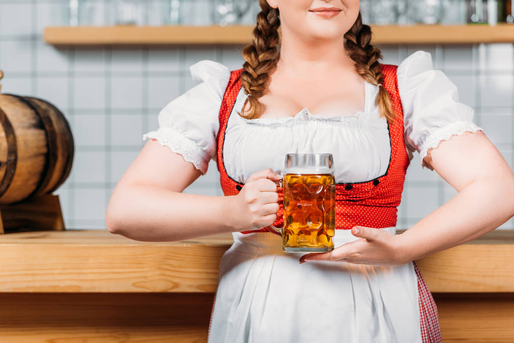 ausgeschnittenes Bild eines Oktoberfest-Barkeepers in bayerischer Tracht mit einem Becher Leichtbier neben der Theke - Foto, Bild
