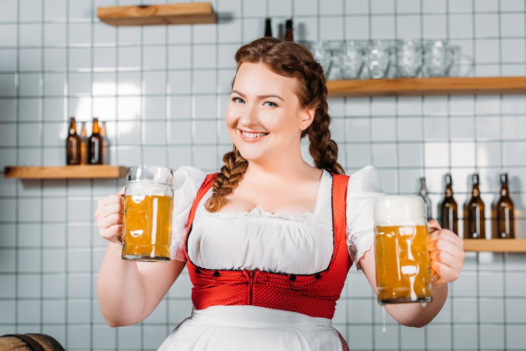 felice cameriera oktoberfest in abito tradizionale bavarese che mostra tazze di birra leggera vicino al bancone del bar
 - Foto, immagini