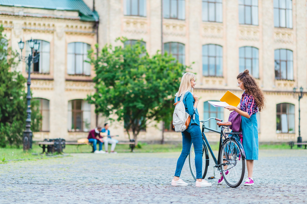 students with bicycle and notebooks standing on street near university - Photo, Image