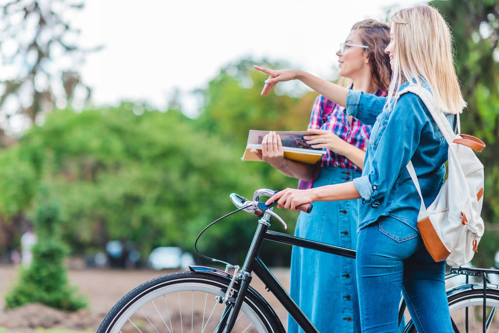 Widok z boku młodej kobiety z rowerów od wskazującego z kolega w pobliżu przez na ulicy - Zdjęcie, obraz