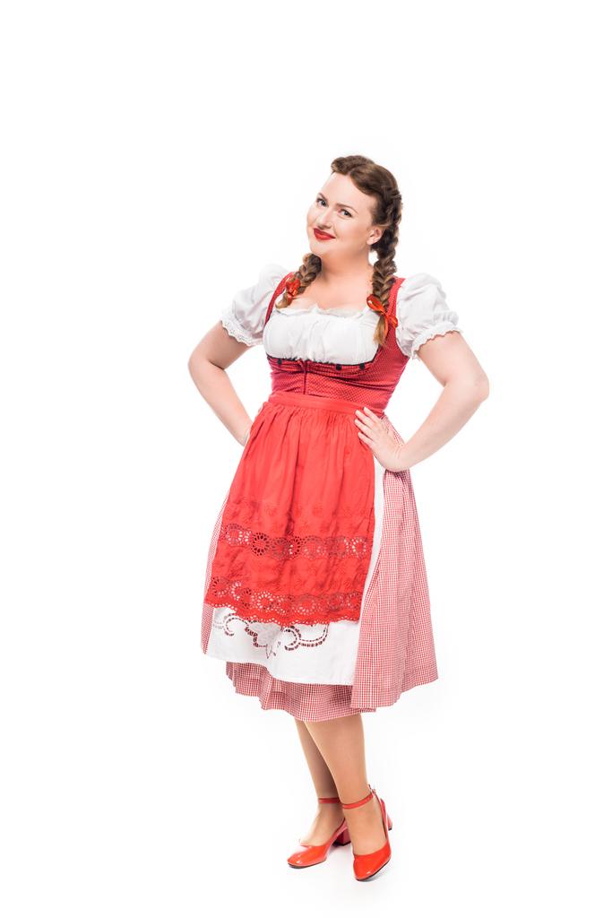 glimlachend oktoberfest serveerster in traditionele Beierse jurk met handen op taille geïsoleerd op witte achtergrond - Foto, afbeelding