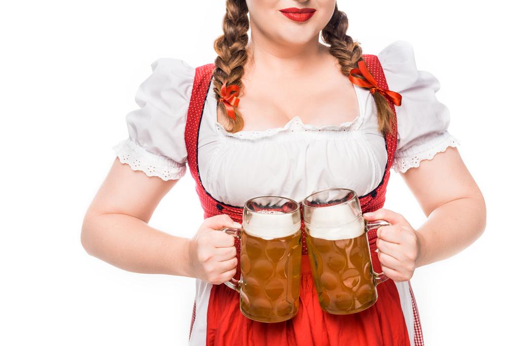 abgeschnittenes Bild einer Oktoberfestkellnerin in bayerischer Tracht, die auf weißem Hintergrund vereinzelt Krüge mit hellem Bier zeigt - Foto, Bild