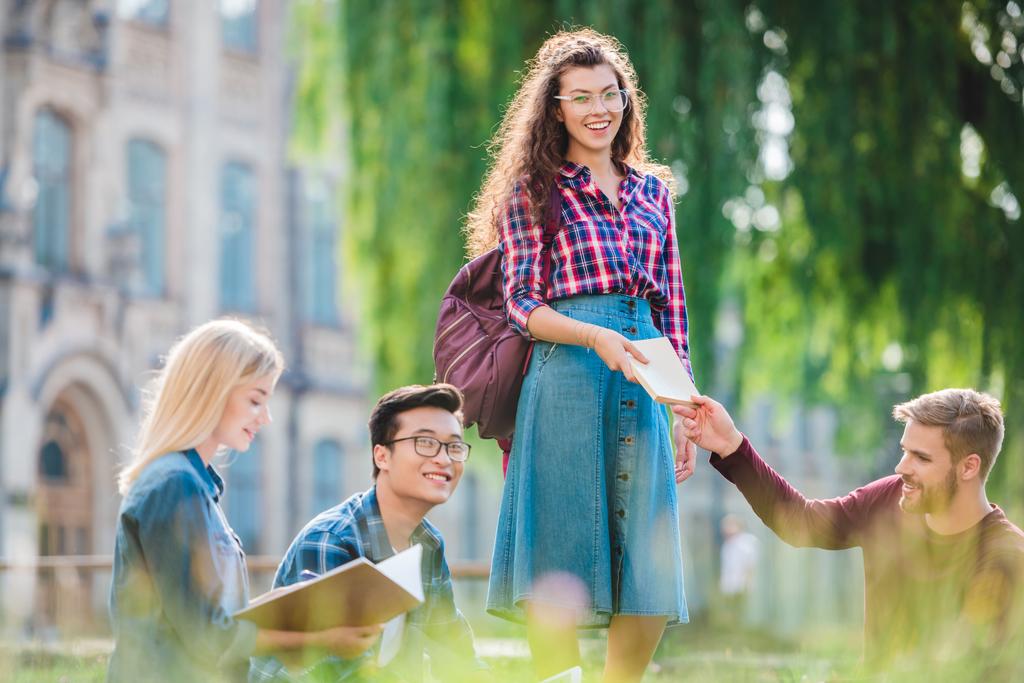 многорасовые студенты, обучающиеся в парке с университетом на фоне
 - Фото, изображение