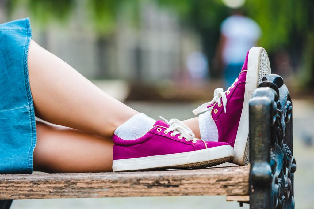 vista parcial de la mujer en zapatos morados descansando en banco de madera en la calle
 - Foto, imagen