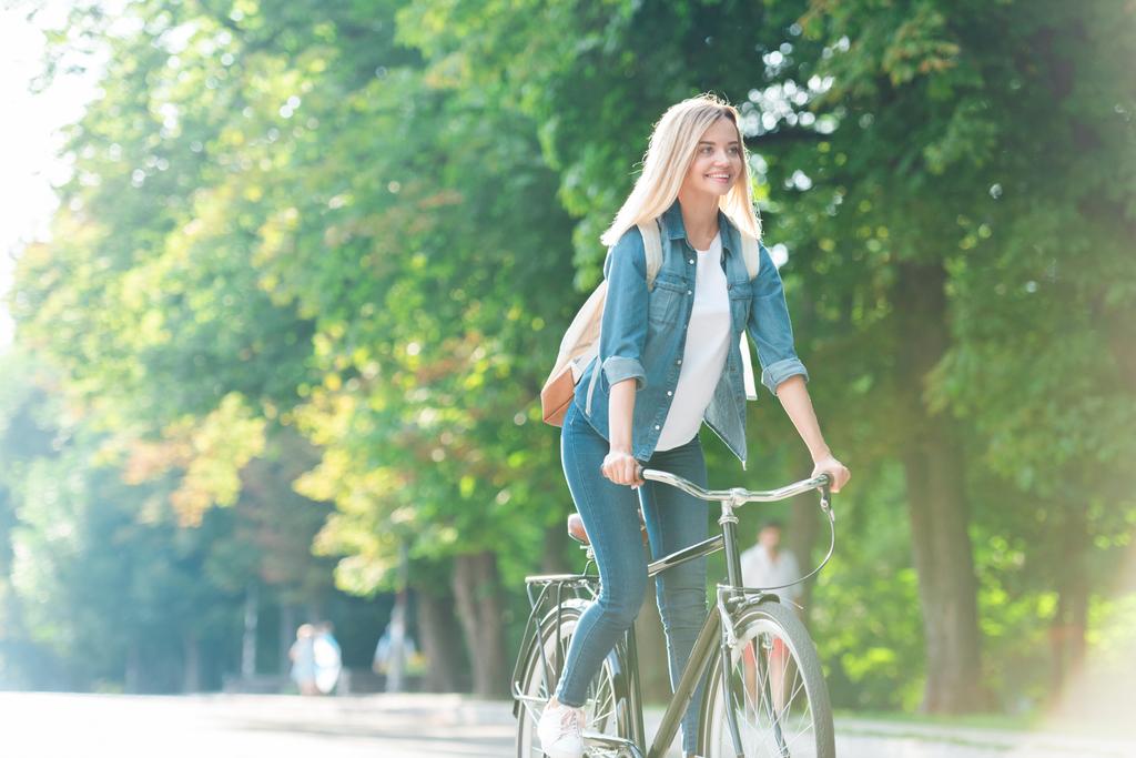 glimlachend student met rugzak fiets op straat - Foto, afbeelding