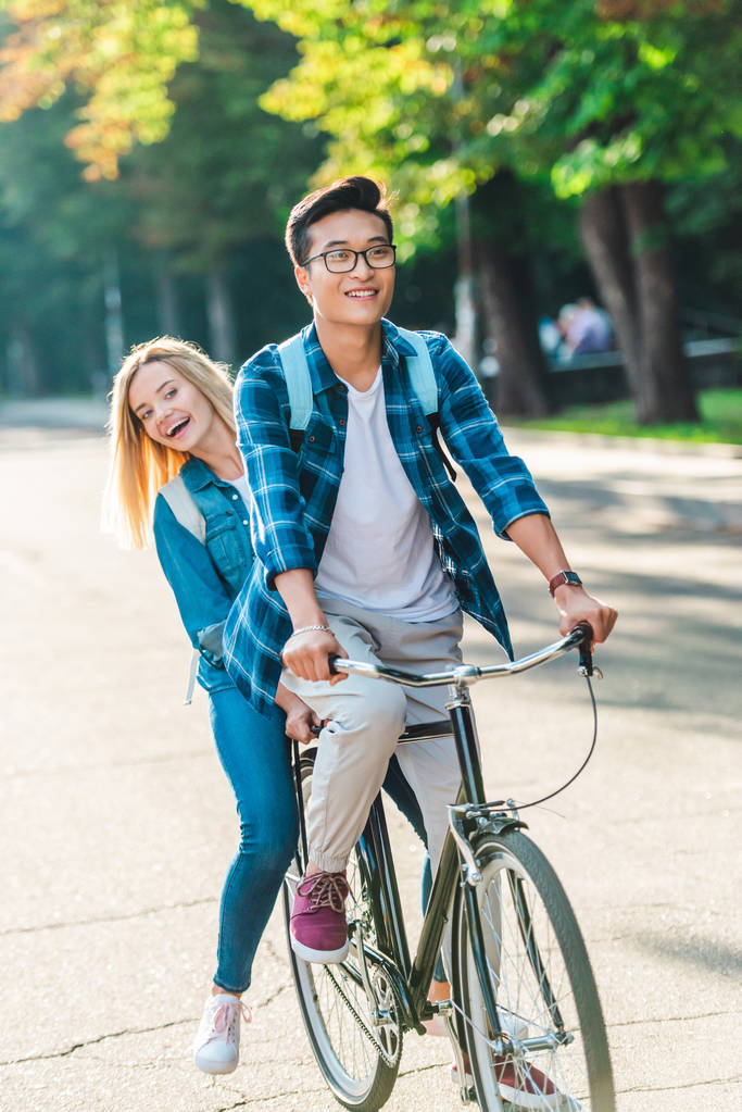 happy multiethnic students riding bicycle together on street - Photo, Image