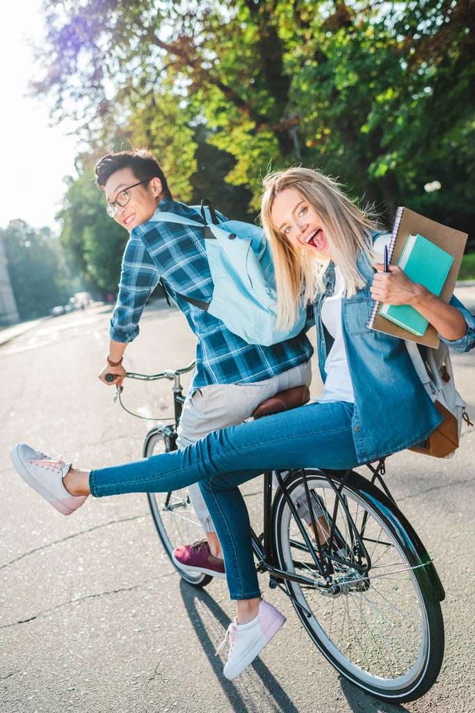 fröhliche multirassische Studenten, die gemeinsam auf der Straße Fahrrad fahren - Foto, Bild
