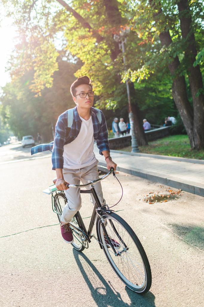 asiático estudiante en gafas con mochila a caballo bicicleta en la calle
 - Foto, imagen