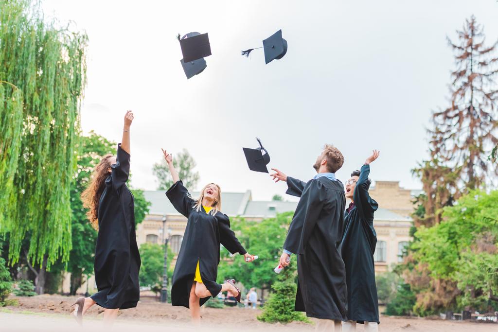 щасливі мультикультурні випускники з дипломами кидають шапки в парк
 - Фото, зображення