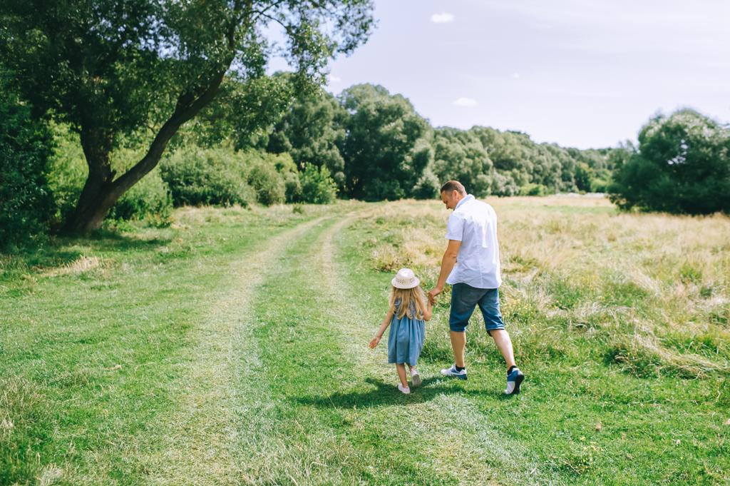 Vista trasera del padre cogido de la mano con su hija y caminando en el campo - Foto, imagen