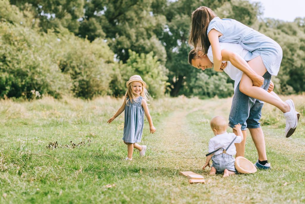 family with children spending time on summer feild, father piggybacking mom - Photo, Image