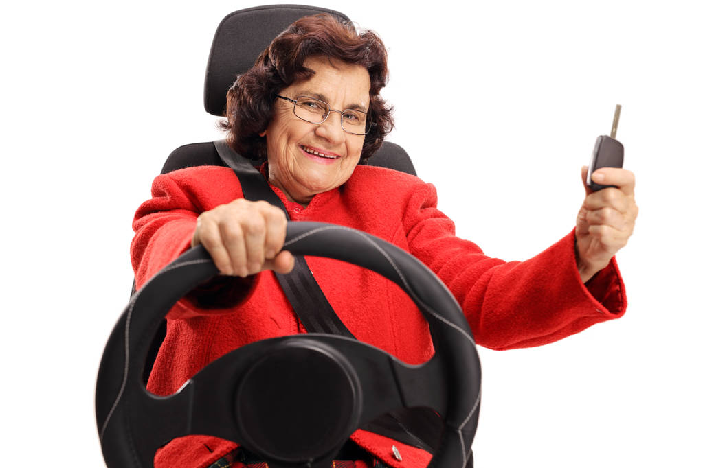 Señora mayor conduciendo y mostrando una llave de coche aislada sobre fondo blanco
 - Foto, imagen