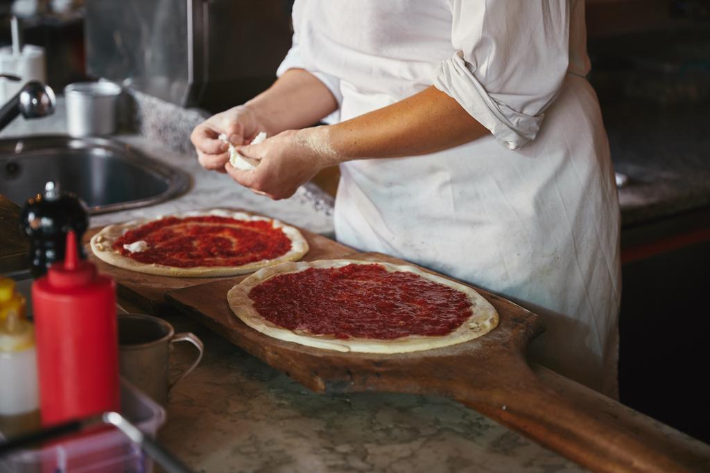 Schnappschuss von Koch, der in Restaurantküche Käsestücke auf Pizza legt - Foto, Bild