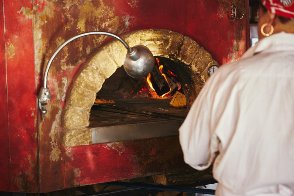 обрізаний знімок шеф-кухаря, який приймає піцу з цегляної печі на кухні ресторану
 - Фото, зображення