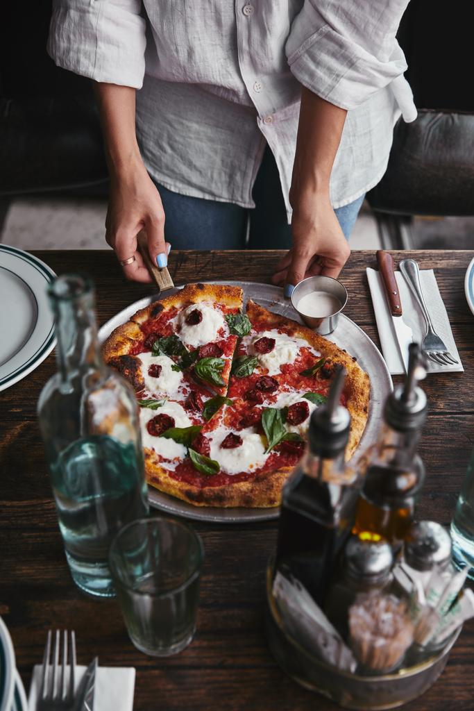 bijgesneden schot van serveert heerlijke pizza op restaurant tafel met water - Foto, afbeelding