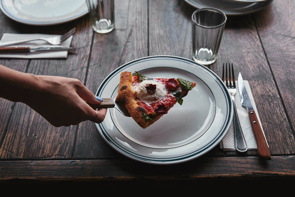 обрезанный снимок женщины, подающей ломтик пиццы Маргарита на тарелке в ресторане
 - Фото, изображение