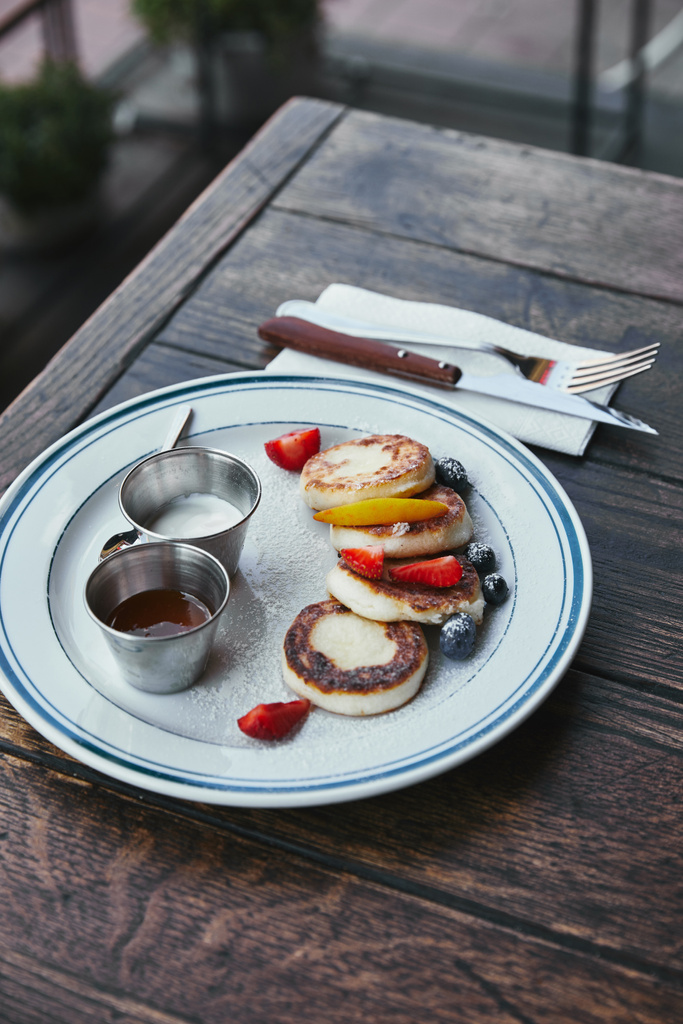 Nahaufnahme von leckeren Quark-Pfannkuchen mit Schalen voller Dippings und Besteck auf dem Holztisch - Foto, Bild