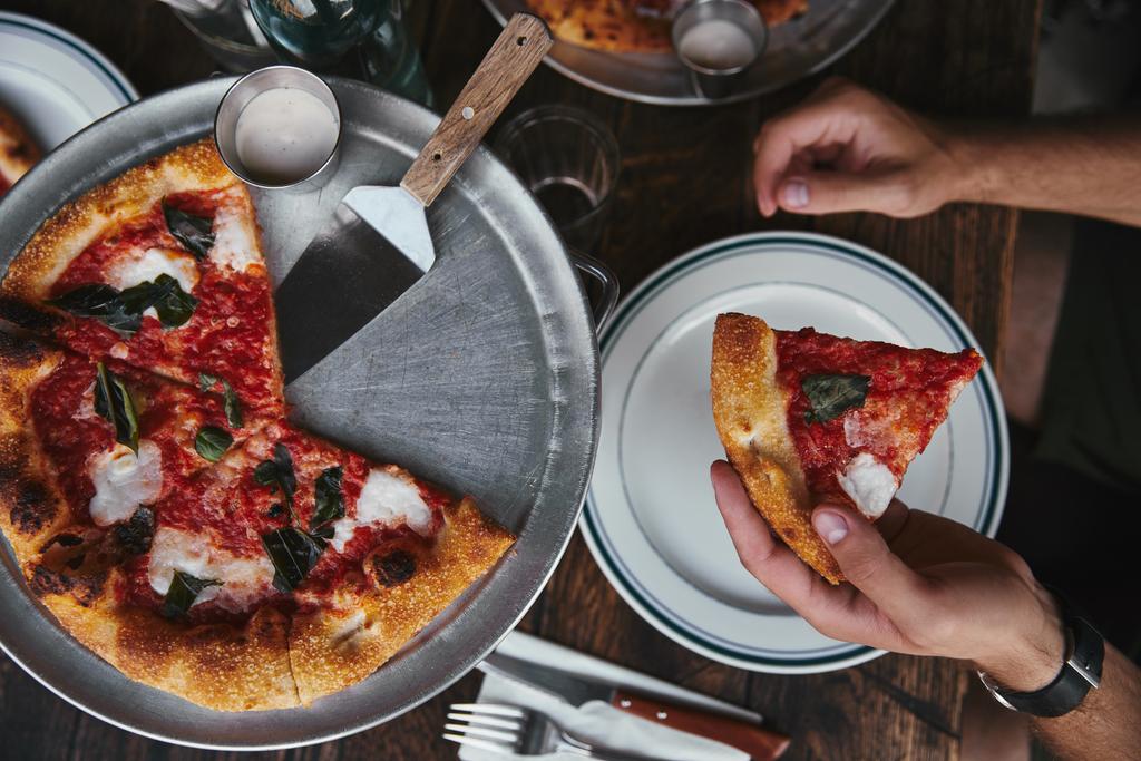 обрезанный снимок человека, поедающего свежеиспеченную пиццу Маргарита в ресторане
 - Фото, изображение
