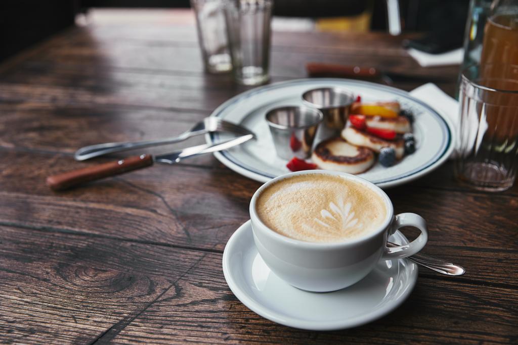 крупним планом знімок сирних млинців на тарілці та чашці кави на сільському дерев'яному столі
 - Фото, зображення