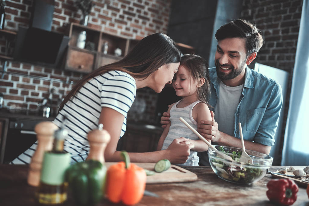 Mami, táta a dcera vaří v kuchyni. Šťastný rodinný koncept. Pohledný muž, atraktivní mladá žena a jejich roztomilá dcerka spolu dělají salát. Zdravý životní styl. - Fotografie, Obrázek