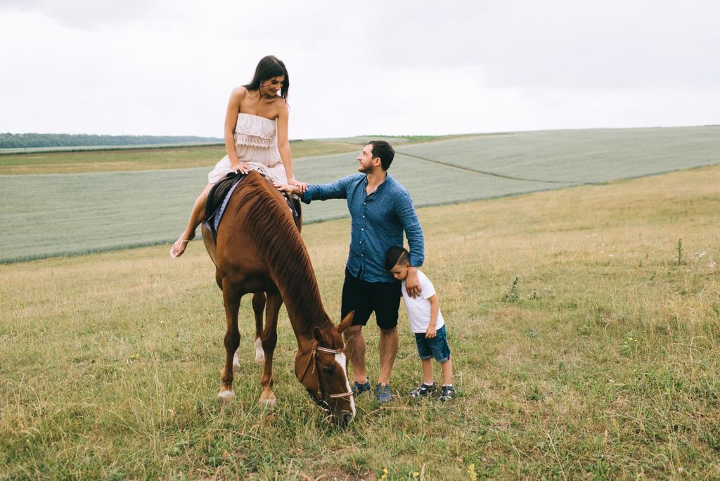 mother riding brown horse, father and son standing on field - Photo, Image
