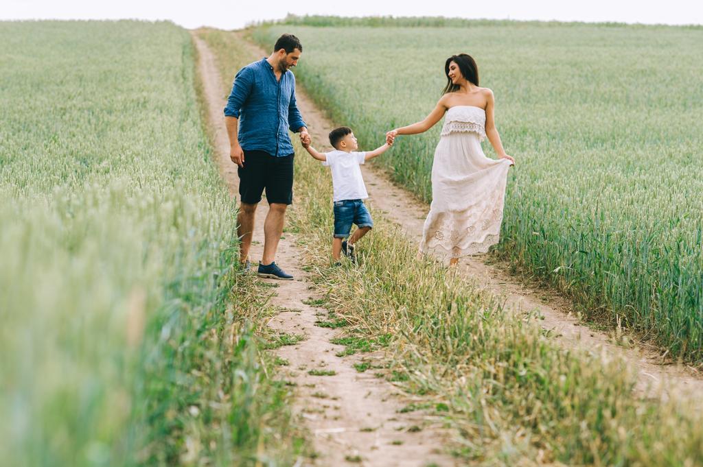 szülők és fia kézenfogva és gyaloglás együtt a kerti ösvény-ban mező - Fotó, kép