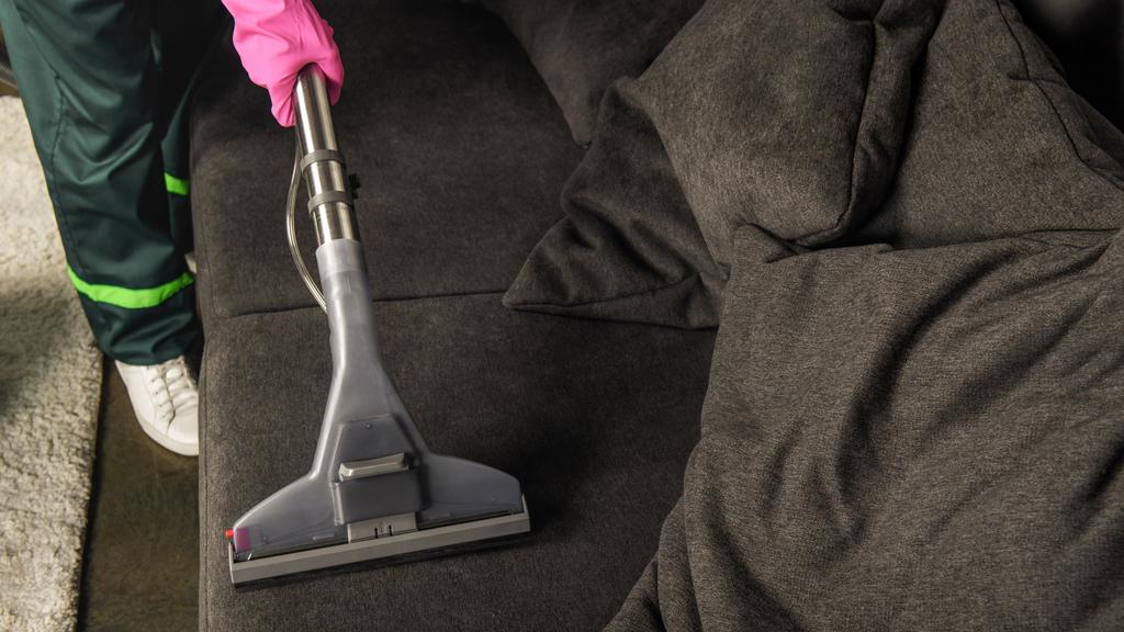 gedeeltelijke weergave van persoon in rubberen handschoen sofa met de stofzuiger schoonmaken  - Foto, afbeelding